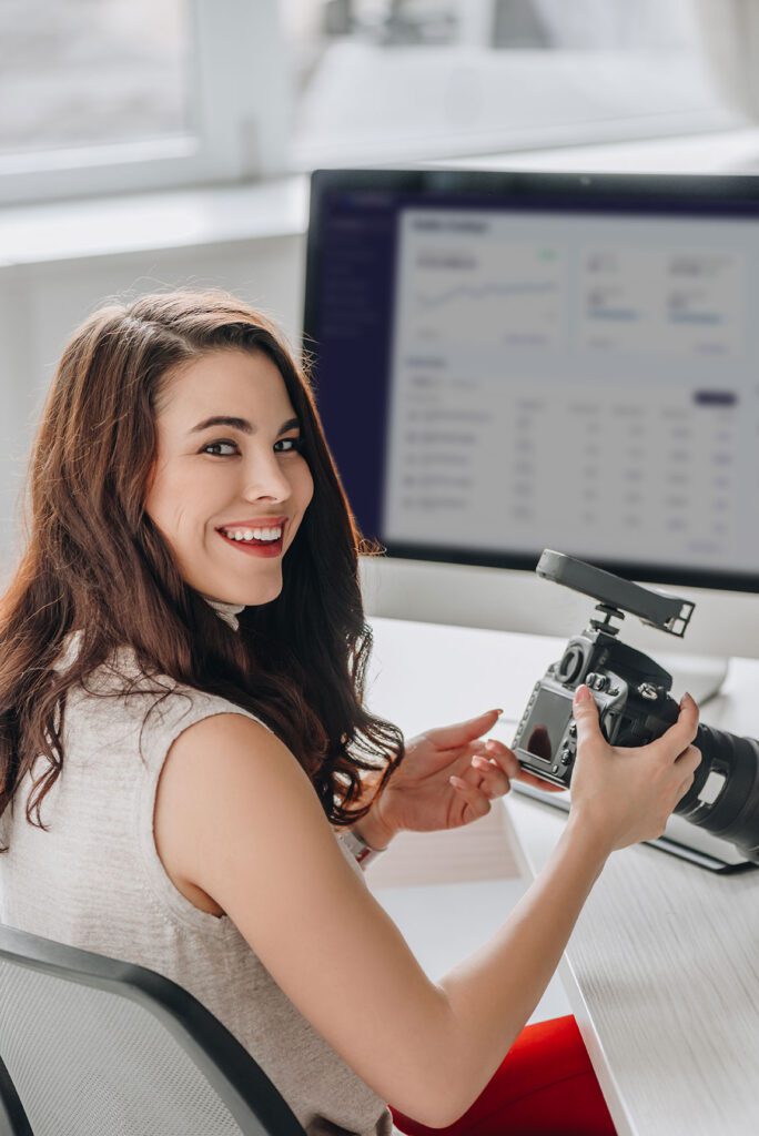 Photographer sitting at a table with a digital camera and photo editing tools, smiling while working.