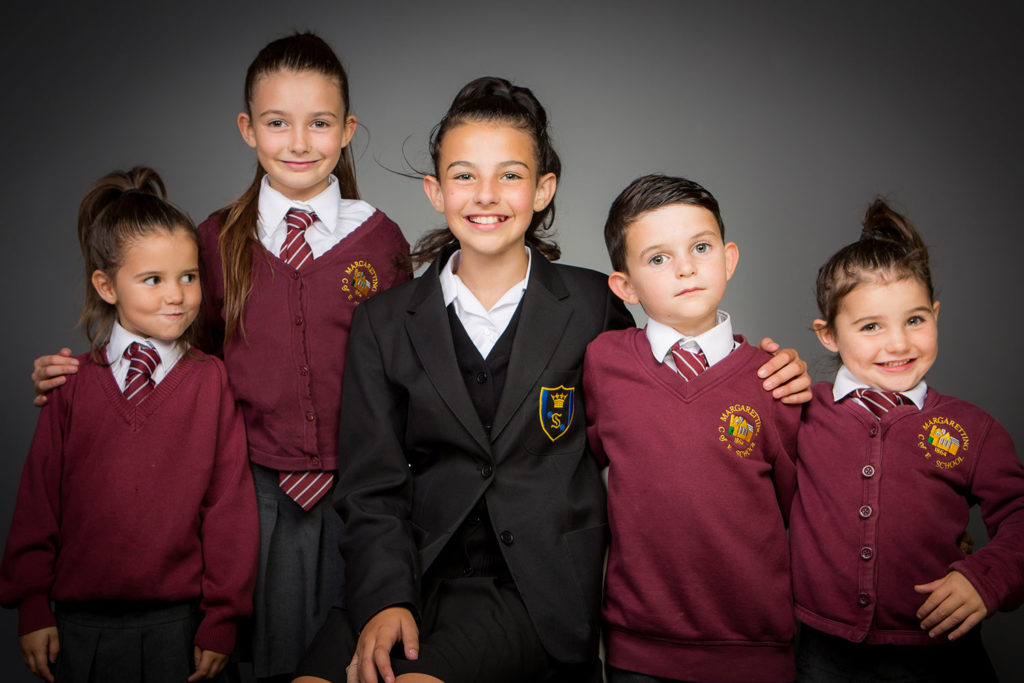 Five children stand together smiling in school uniforms